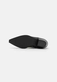 Semelle de chaussure en cuir présentant un design lisse et pointu avec une surface noire plate et une légère accentuation grise au bord du talon.