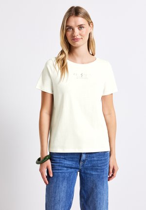 T-shirt à manches courtes, jaune clair en coton, avec un col rond et un texte imprimé discret sur le devant. Associé à un jean en denim bleu.