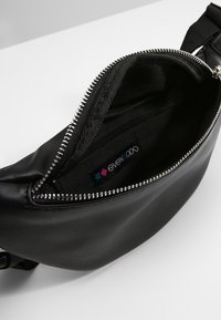 Borsa a tracolla nera in pelle con zip argentata aperta, che mostra l'interno in tessuto e l'etichetta del marchio all'interno su uno sfondo bianco.