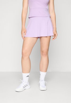 Lilac activewear top with matching pleated skirt. Shoes are white with gray accents and black logo. Model wears white athletic socks.