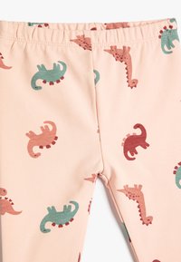 Leggings rosas con un divertido patrón de dinosaurios en verde y rojo, con una cinturilla elástica y una textura de tela suave y elástica.