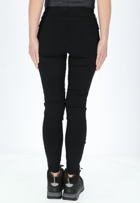Svarta leggings med ett slätt, elastiskt material; hög midje-design; sömmar på baksidan; bärs med svarta träningsskor.