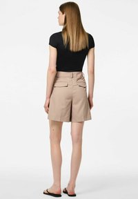 T-shirt noir ajusté associé à un short beige sur mesure présentant deux poches arrière et un ourlet qui atteint le milieu de la cuisse. Texture du tissu lisse.