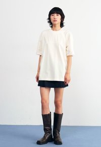 Cremefarget oversized t-skjorte med korte ermer, sammen med et svart skjørt og brune støvler til kneet. Enkel og minimalistisk design.