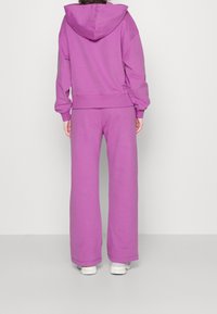 Purple hoodie and wide-leg pants made of soft fabric. Hoodie features a large hood and ribbed cuffs. Versatile casual set view from behind.