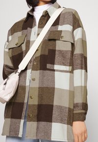 Ruudullinen paita vihreän, ruskean ja vaaleansinisen sävyissä. Pehmeä kangas, jossa on kaksi rintataskua ja napitus. Yhdistetty vaalean laukun kanssa.