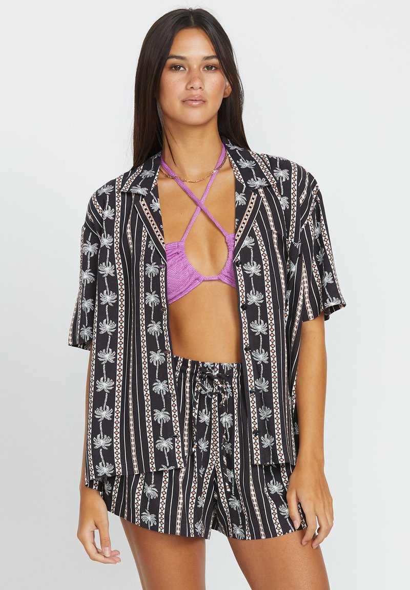 Chemise à rayures noires et blanches avec un motif de palmier, assortie à un bikini texturé violet. Coupe ample, manches courtes et shorts assortis.