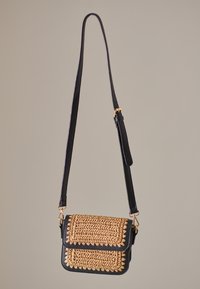 Sort crossbody-taske med tekstureret, vævet gulddetalje på klappen, justerbar rem og guldfarvede hardware-detaljer.