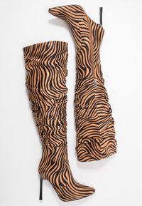 Botas de hasta la rodilla con estampado de cebra fabricadas en un tejido suave y texturizado. Con punta afilada, alto tacón de aguja y cremallera lateral para el cierre.