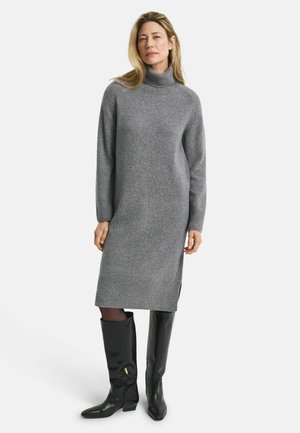 Graues gestricktes Rollkragenkleid mit langen Ärmeln, seitlichen Schlitzen und geripptem Saum. Kombiniert mit kniehohen schwarzen Lederstiefeln.
