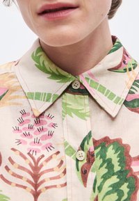 Mehrfarbiges Hemd mit einem Blumenmuster in Grün, Rosa und Beige. Verfügt über einen spitzen Kragen und eine Knopfleiste. Natürliche Stoffstruktur.