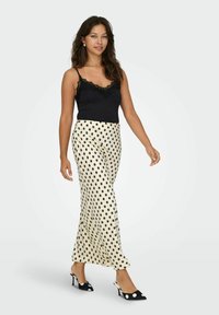 Musthave mustripsiga must pitsääristega kampsun koos kreemja seelikuga, millel on suured mustad täpid. Mudel kannab musta ja valge täpikaga kontsakingi.