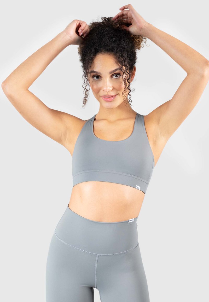 Szary biustonosz sportowy i pasujące legginsy wysokiej talii wykonane z elastycznego materiału. Charakteryzują się okrągłym dekoltem i elastycznym paskiem na dole.