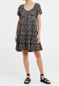 Musta mekko, jossa on kukkakuosi, lyhyet hihat, v-pääntie, nappi yksityiskohtia ja kerroksellinen volangihelma. Yhdistetty mustien hihnatossujen kanssa.