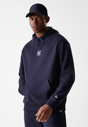 Navy blue hoodie with a front pocket, drawstring hood, and white logo. Matching cap complements the outfit, featuring a streamlined design.