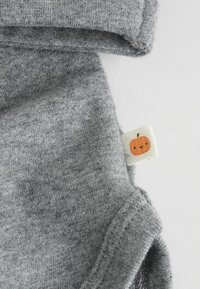 Nærbillede af grå strikket stof med et lille hvidt mærke, der har en smilende orange græskarillustration.
