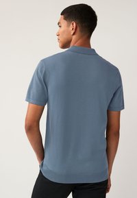 Polo shirt azzurro chiaro a maniche corte con finitura a maglia testurizzata, caratterizzato da un colletto classico e orlo a coste. Design minimalista.