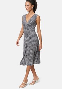 Navy sleeveless dress with a deep V-neck, featuring a geometric pattern and a flowing A-line skirt, paired with beige heeled sandals.