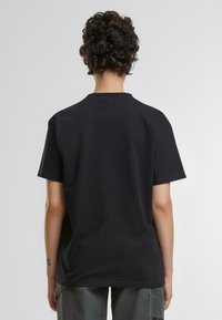 Camiseta de algodón negra con cuello redondo, mangas cortas y un corte relajado. La tela es suave, sin gráficos ni patrones visibles.
