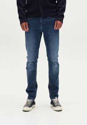 Dunkelblaue Jeans im Slim-Fit, mit einem klassischen Fünf-Taschen-Design und dezentem Ausbleichen. Kombiniert mit schwarzen High-Top-Sneakers.