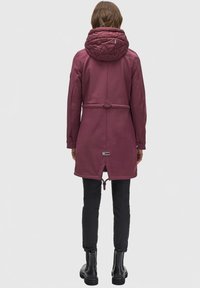Maroon waterproof jacket with a quilted hood, cinched waist, and drawstring details. Worn over black pants and boots.