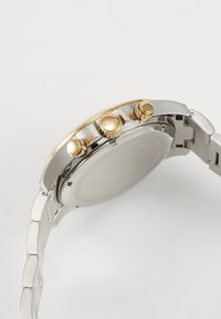 Orologio in tonalità argento e oro con bracciale in acciaio inossidabile. Presenta tre pulsanti e una corona testurizzata, con un quadrante argento liscio.