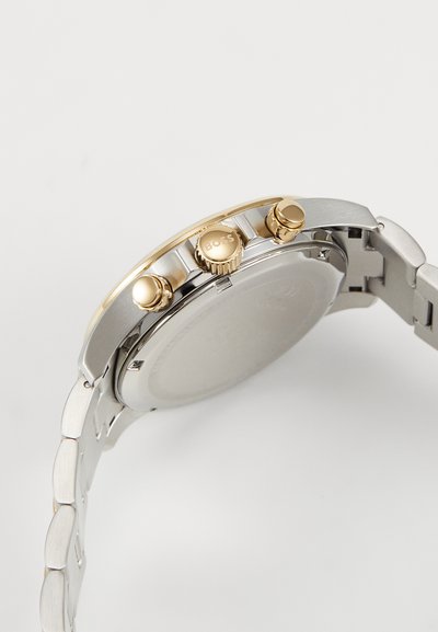 Montre argentée et dorée avec un bracelet en acier inoxydable. Comprend trois poussoirs et une couronne texturée, avec un cadran argenté lisse.