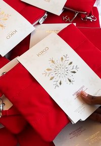 Røde polstrede kosmetikkposer med sølvglidelåser, ledsaget av hvite kort med gullbokstaver og et snøflakedesign.