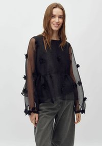 Must mustriga pluus tekstureeritud kangast, pikkade varrukatega, lillemotiividega ning peplum taljega. Kandmiseks hallide pükste peal.