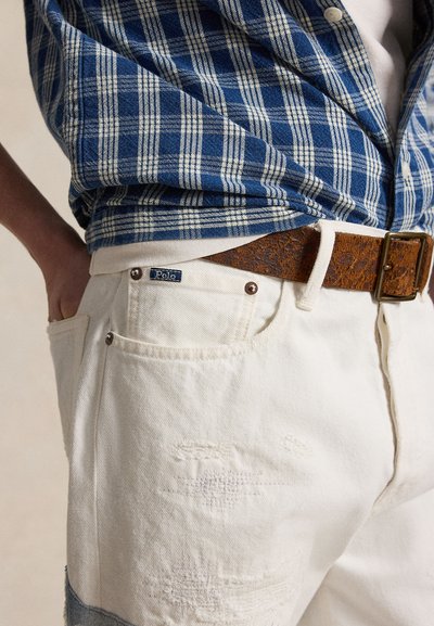 Άσπροι ανδρικοί τζιν με φθαρμένη όψη και ετικέτα Polo, συνδυασμένοι με καφέ δερμάτινη ζώνη με υφή και μπλε καρό πουκάμισο, που είναι μέσα στη μέση.