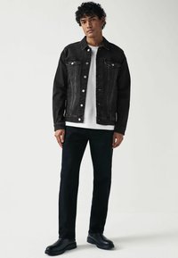 Schwarze Jeansjacke mit zwei Brusttaschen, darunter ein weißes Hemd, kombiniert mit schwarzen Hosen und schwarzen Stiefeln; gerade geschnitten, strukturiertes Material.