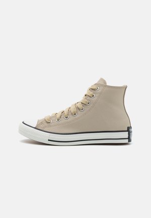 Sneaker alta beige in canvas, con punta in gomma bianca, chiusura con lacci e superficie testurizzata con accenti scuri sulla suola e sul logo.