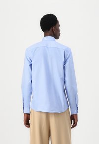 Camisa de manga larga de color azul claro en un tejido suave, con cuello abotonado, yugo trasero, y puños con pequeños botones.