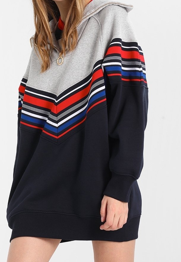 Sweat à capuche gris et bleu marine, présentant un motif chevron avec des rayures rouges, bleues et noires. Fabriqué en tissu doux avec des poignets côtelés.
