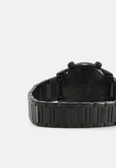 Black analog watch with a steel band, featuring a matte finish, rectangular links, and a round black dial with two side buttons.