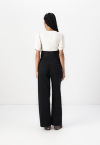 Light beige ribbed short-sleeve top with a fitted black waistband and black wide-leg jeans, paired with leopard print heels.