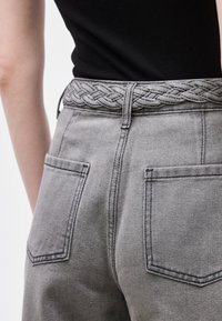 Άτομο που φοράει γκρι τζιν παντελόνι με τσέπες με επιδιορθώσεις και πλεκτή γκρι ζώνη, συνδυασμένο με μαύρο εφαρμοστό τ οπ.