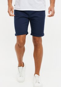 Marineblaue Shorts mit umgekrempeltem Saum aus atmungsaktivem Stoff, mit einer glatten Textur und einer taillierten Passform, kombiniert mit weißen Sneakers.