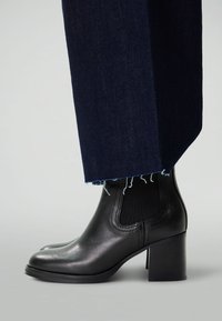 Bottines noires en cuir avec un bout arrondi et un talon bloc. Associées à un pantalon en denim foncé avec un ourlet effiloché et une légère évasement.