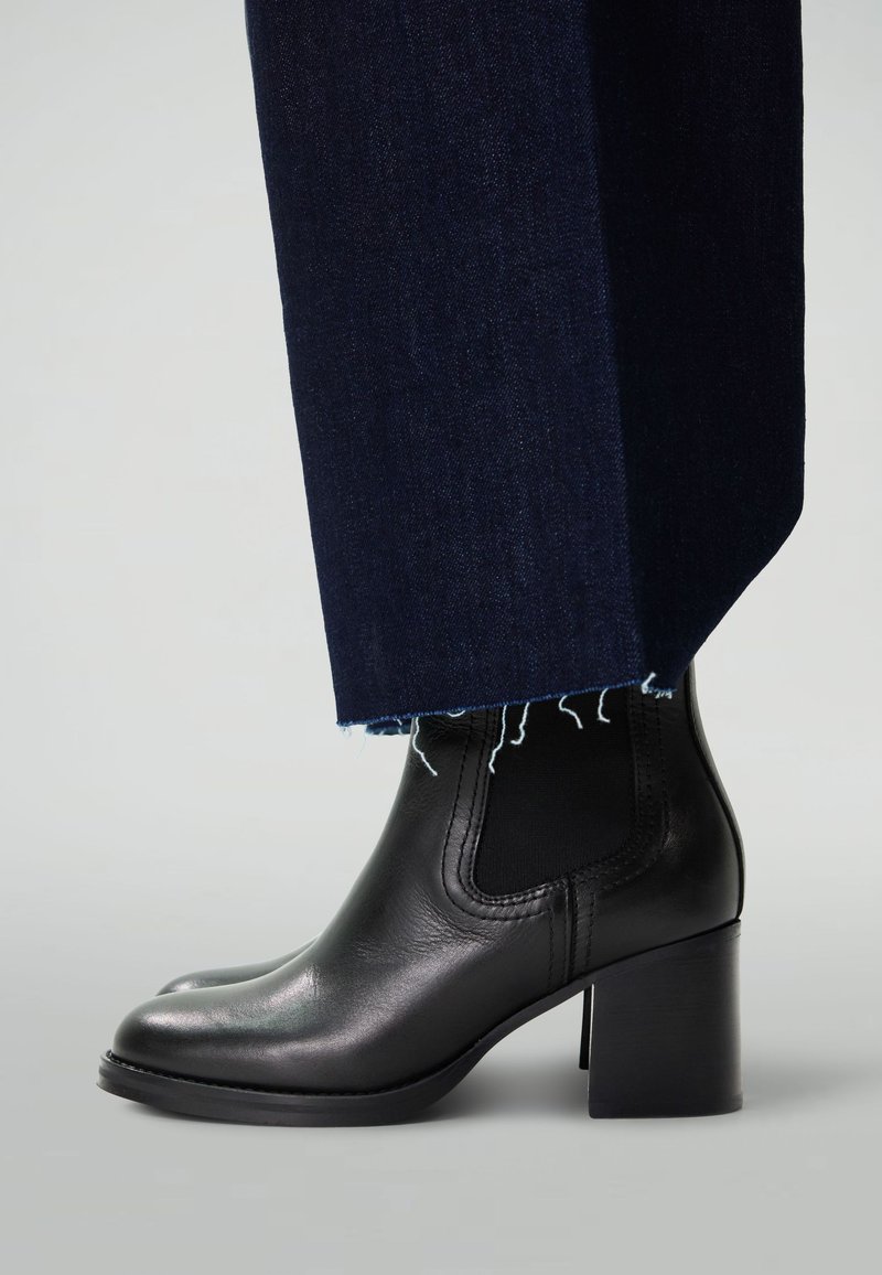 Bottines noires en cuir avec un bout arrondi et un talon bloc. Associées à un pantalon en denim foncé avec un ourlet effiloché et une légère évasement.