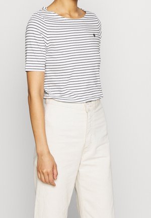 Witte T-shirt met korte mouwen en horizontale zwarte strepen, ronde halslijn en een klein logo op de borst, gecombineerd met lichte broeken.