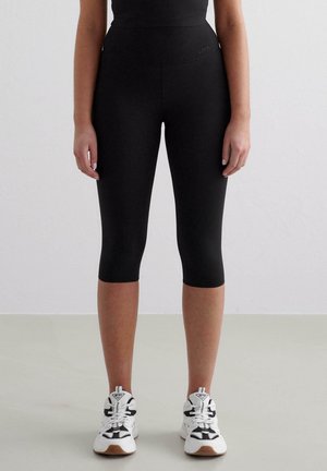 Sorte capri leggings med høy midje, glatt materiale og en tettsittende design, paret med hvite treningstsko.