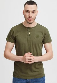 Olivegrünes Kurzarm-Henley-T-Shirt mit rundem Ausschnitt, Knopfleiste und einer strukturierten Logoprint auf der Brust; glattes Baumwollmaterial.