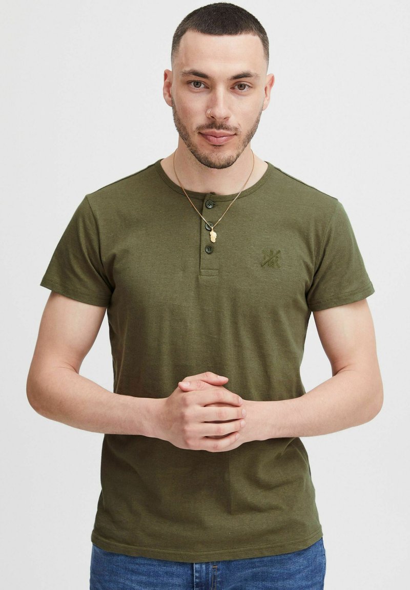 Olivegrünes Kurzarm-Henley-T-Shirt mit rundem Ausschnitt, Knopfleiste und einer strukturierten Logoprint auf der Brust; glattes Baumwollmaterial.