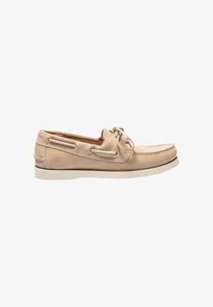 Mocassin beige en daim avec lacets à l'avant, œillets latéraux et semelle en caoutchouc blanche, présenté de profil sur fond blanc.