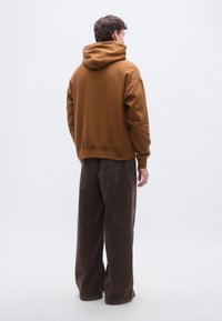 Brun huvtröja med avslappnad passform och ribbad fåll, kombinerad med mörkbruna vida byxor med bakfickor.