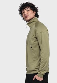 Olivgrüner Pulloverjacke mit hohem Kragen, Reißverschluss vorne und seitlichen Taschen. Weiches Material mit glatter Textur und minimalem Branding.