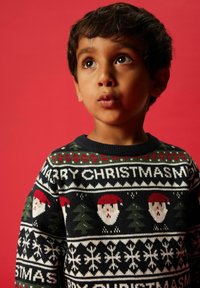 Maglione di Natale lavorato a maglia con facce di Babbo Natale, alberi di Natale e fiocchi di neve in verde scuro, rosso e bianco su uno sfondo nero.