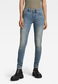 Jeans aderenti blu con aree sbiadite, leggere pieghe e design a cinque tasche, abbinati a stivali neri con suola spessa alla caviglia.
