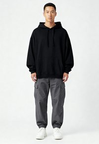 Felpa nera con tasca frontale e cordino, abbinata a pantaloni cargo grigi con tasche laterali, completata da sneakers bianche.